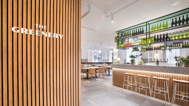 Een moderne bar met houten details, een toog met barstoelen en flessenkasten.