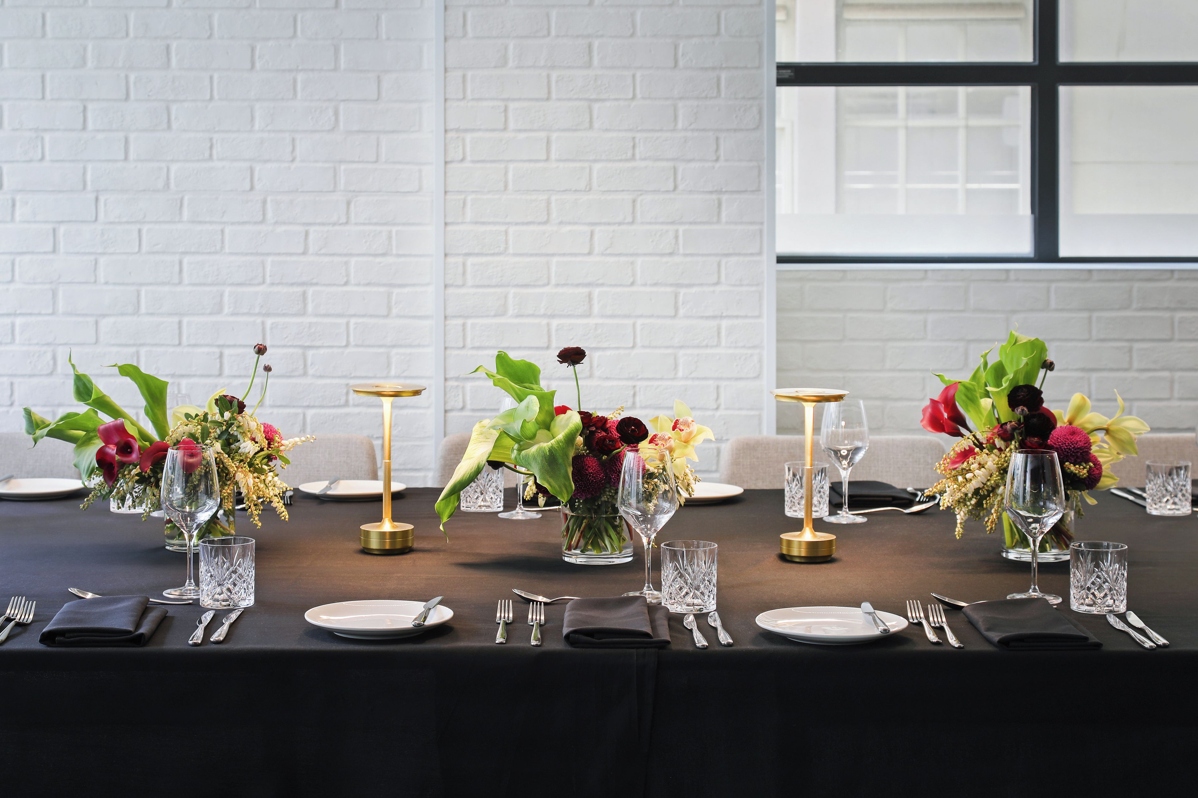 Una mesa de comedor con varios puestos individuales, incluyendo platos, cubiertos y cristalería, dispuestos en fila.