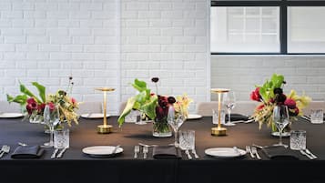 Una mesa de comedor con varios puestos individuales, incluyendo platos, cubiertos y cristalería, dispuestos en fila.