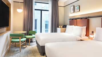A hotel room with two beds, a small table, two chairs, a TV, and a window with curtains.