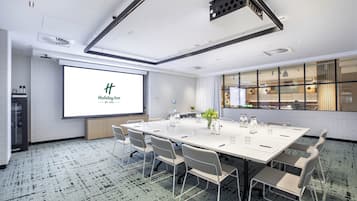 Un salón de conferencias con una larga mesa, sillas, una pantalla de proyector y un ventanal grande.