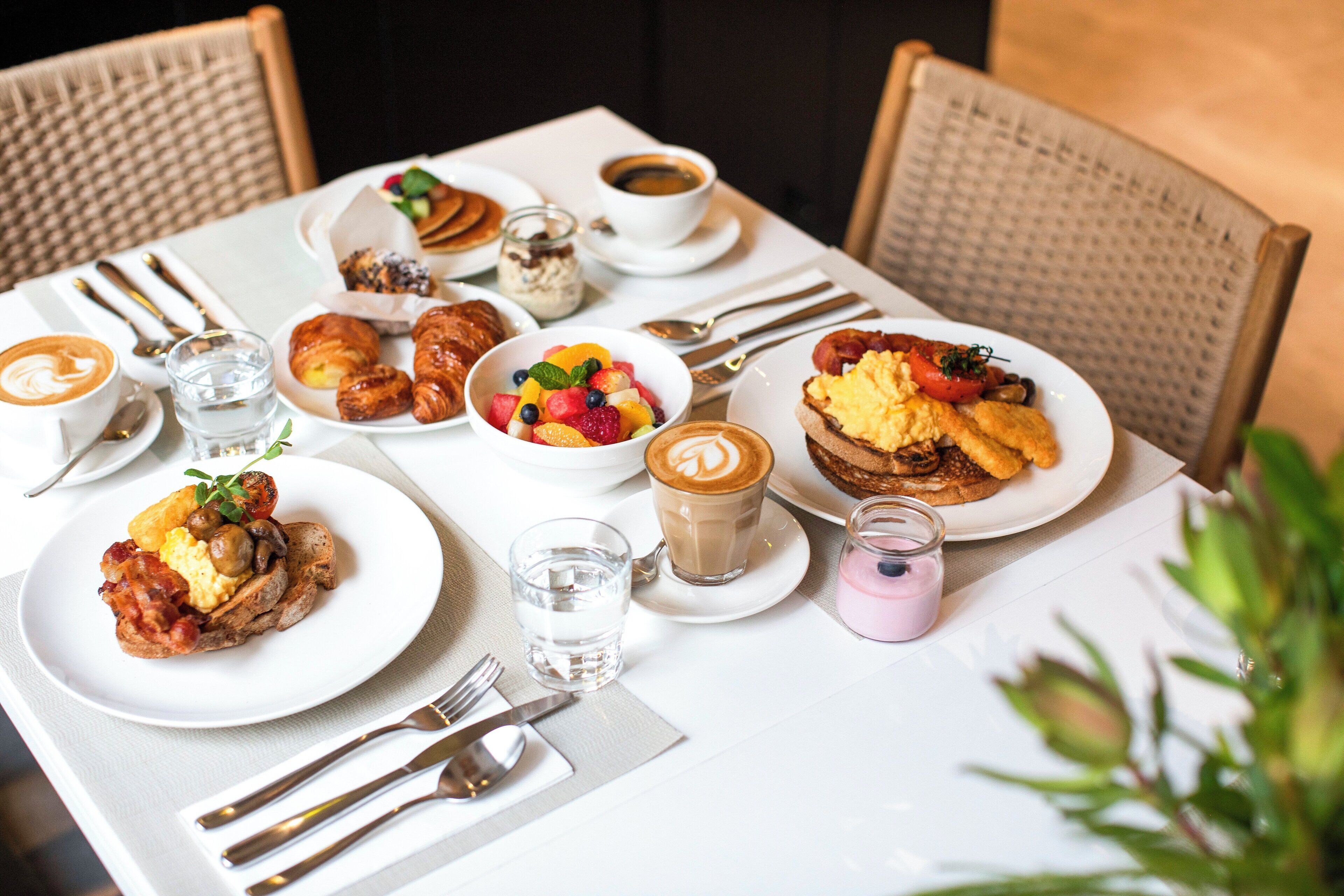 A breakfast setting with croissants, fruit, coffee, and pastries on a table.