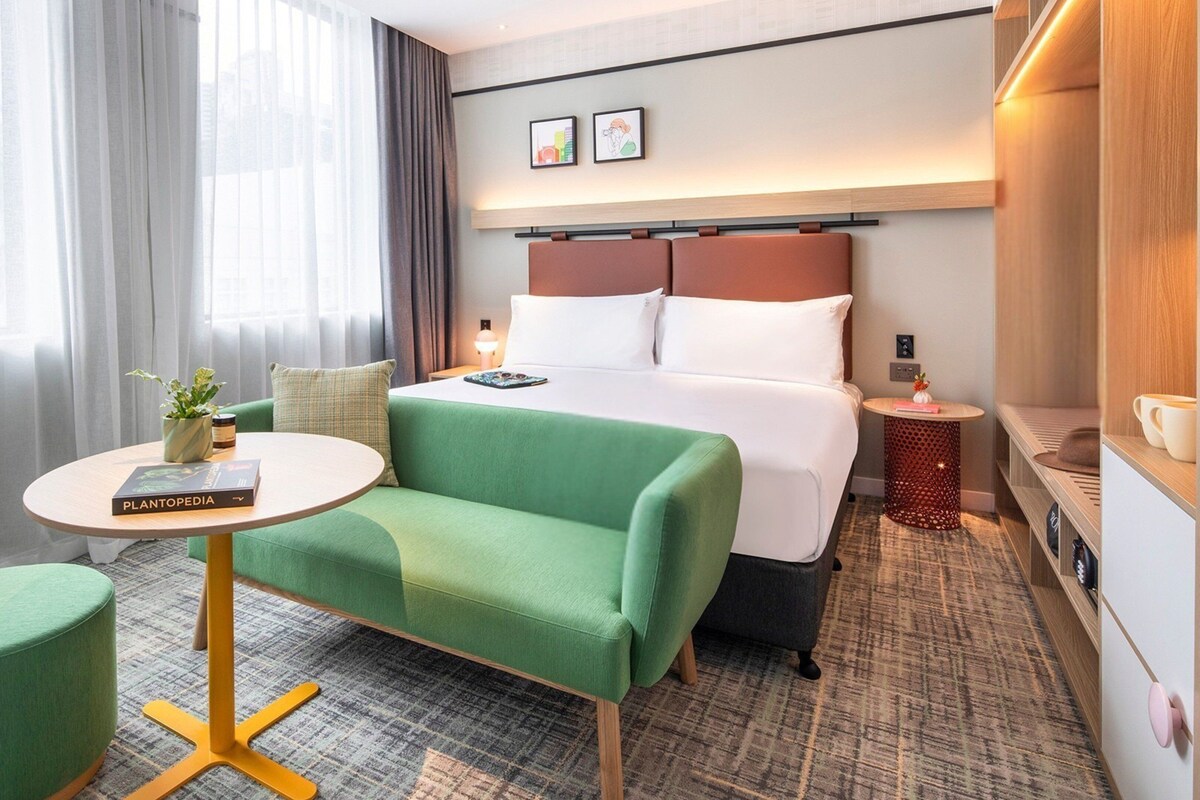Een hotelkamer met een bed, een groene bank, een klein rond tafeltje en een nachtkastje met een lamp.