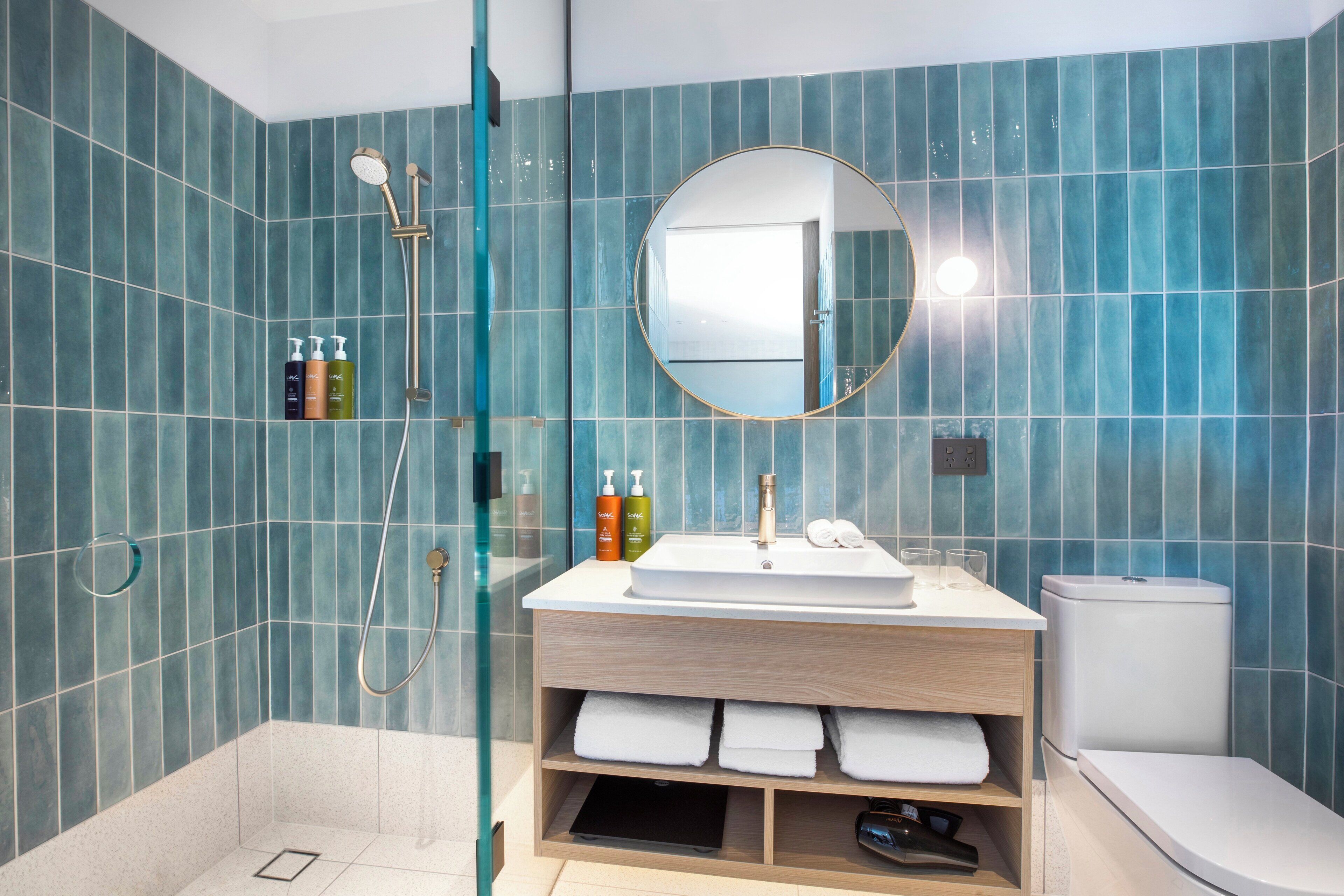 A modern bathroom with blue tiles, a round mirror, a sink, and a toilet.