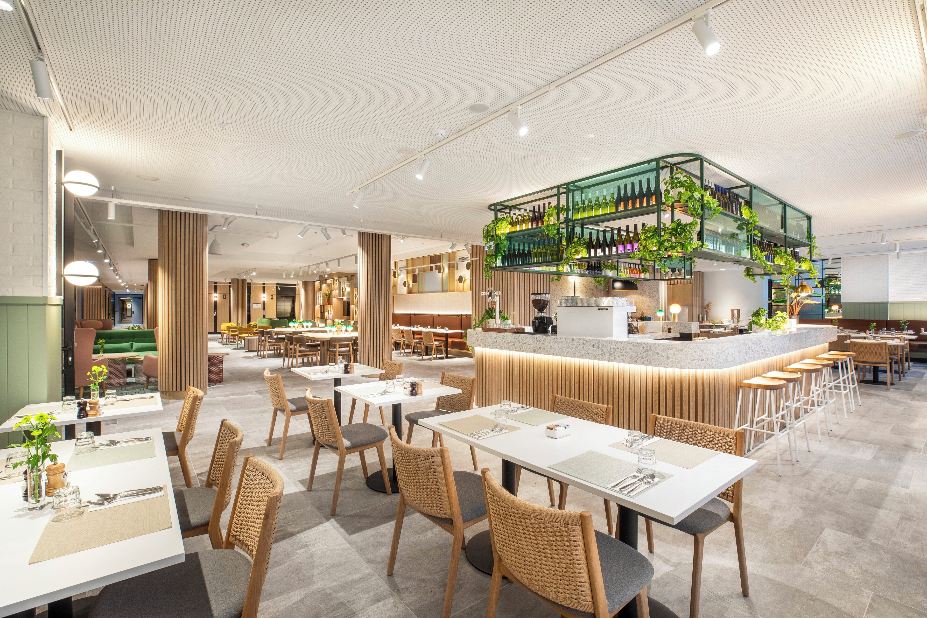 En modern restaurang med en central bardisk, flera matbord och ett varierat utbud av sittplatser.