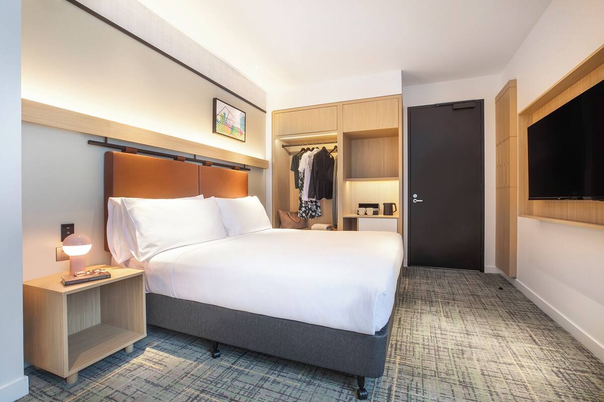 Une chambre d’hôtel comprenant un lit, une table de chevet, une lampe, une armoire et un téléviseur.