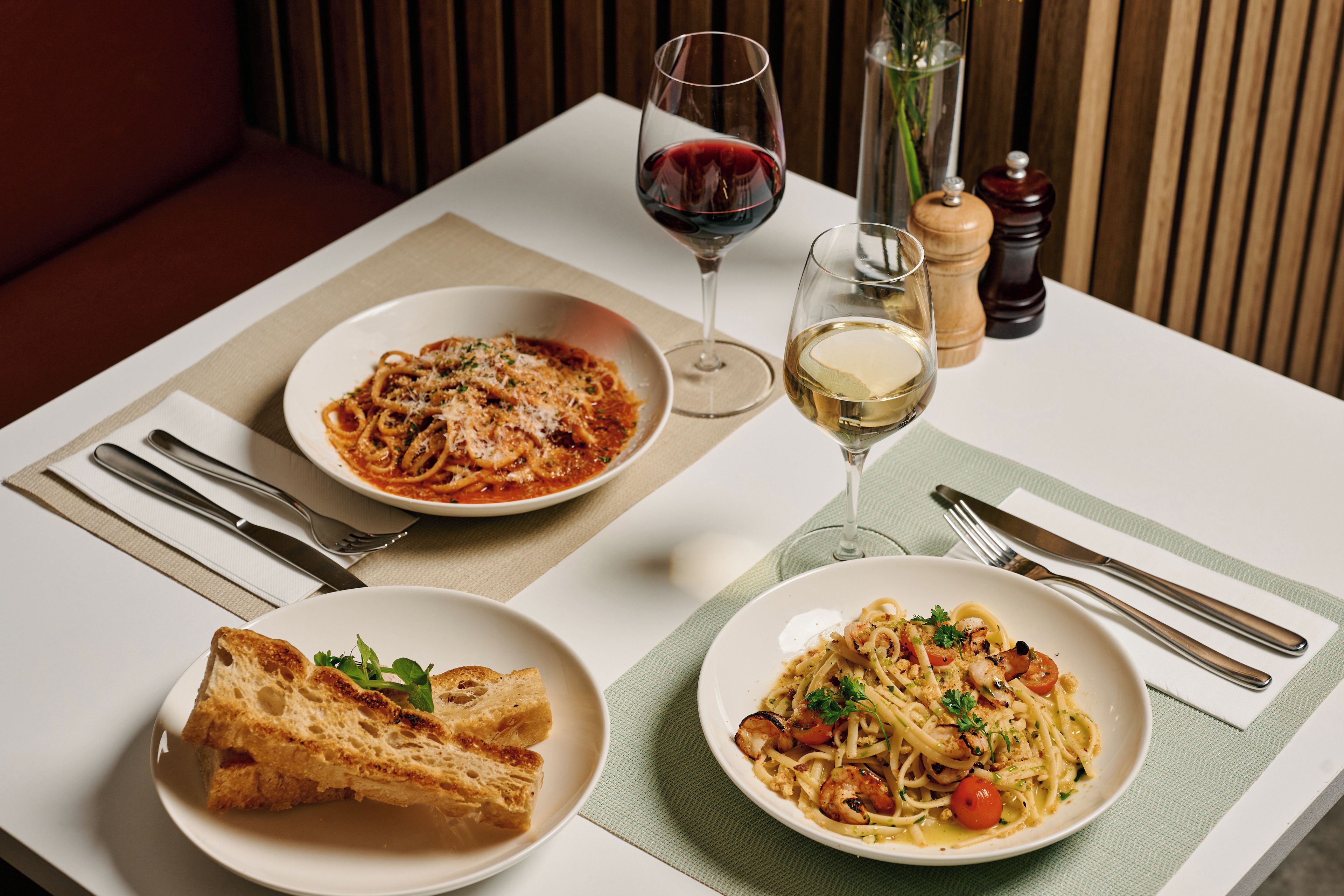 A dining table with two plates of pasta, a glass of red wine, and a glass of white wine.