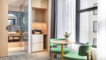 Habitación de hotel moderna con un gran ventanal, una silla verde, una mesita con una planta y un armario empotrado con espejo.