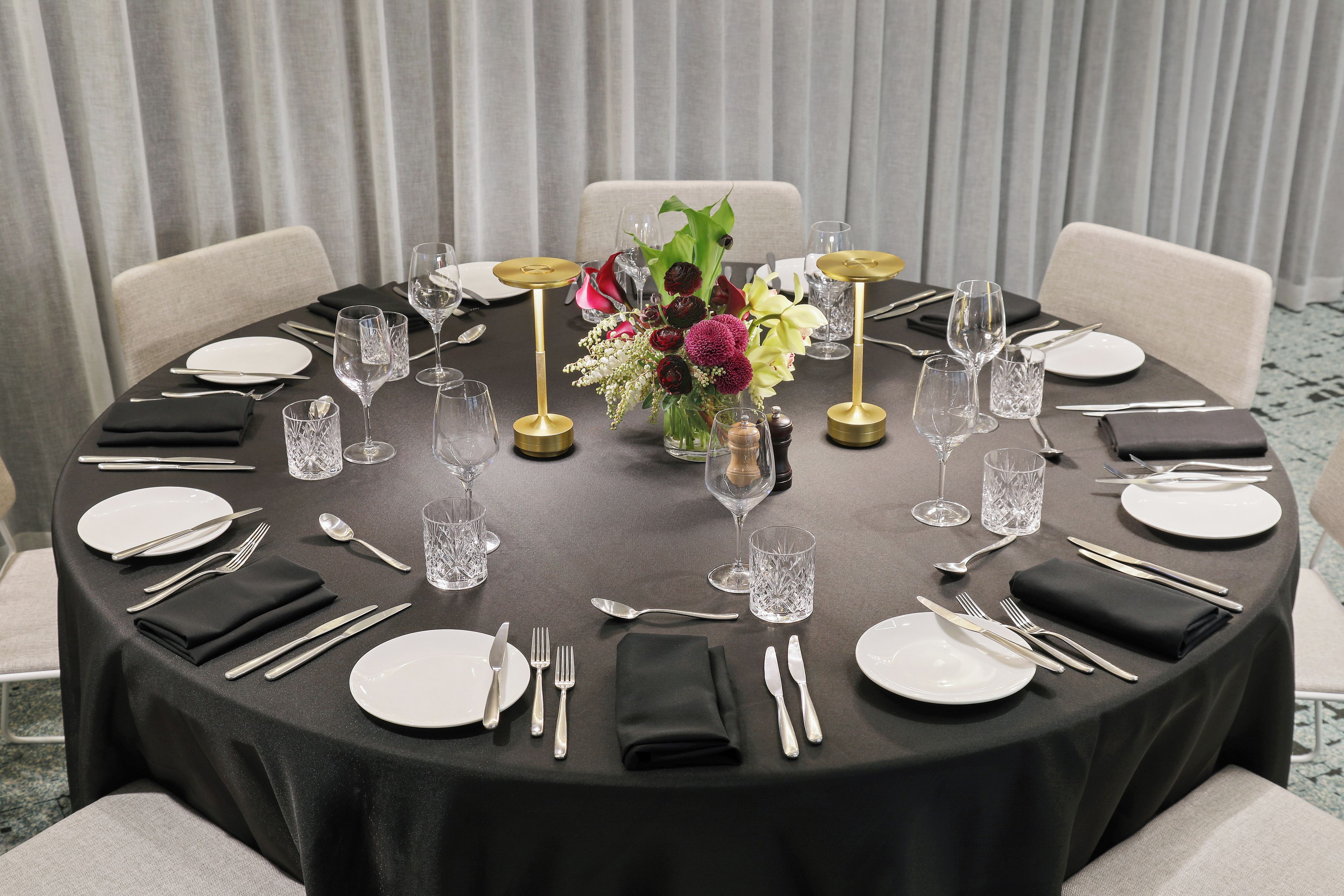 A round table set for a meal with a black tablecloth, white plates, silverware, and clear glassware.
