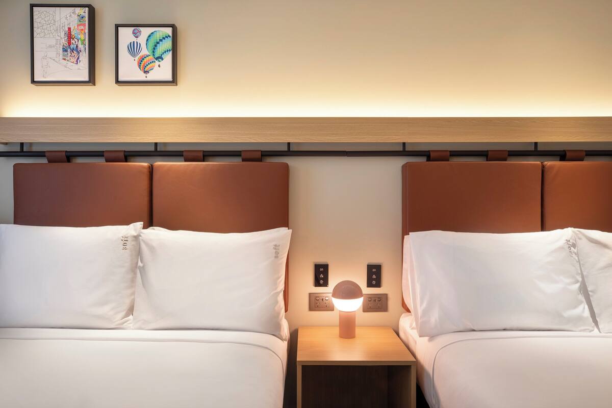 Une chambre d’hôtel avec deux lits, une table de chevet avec une lampe et deux œuvres d’art encadrées au mur.