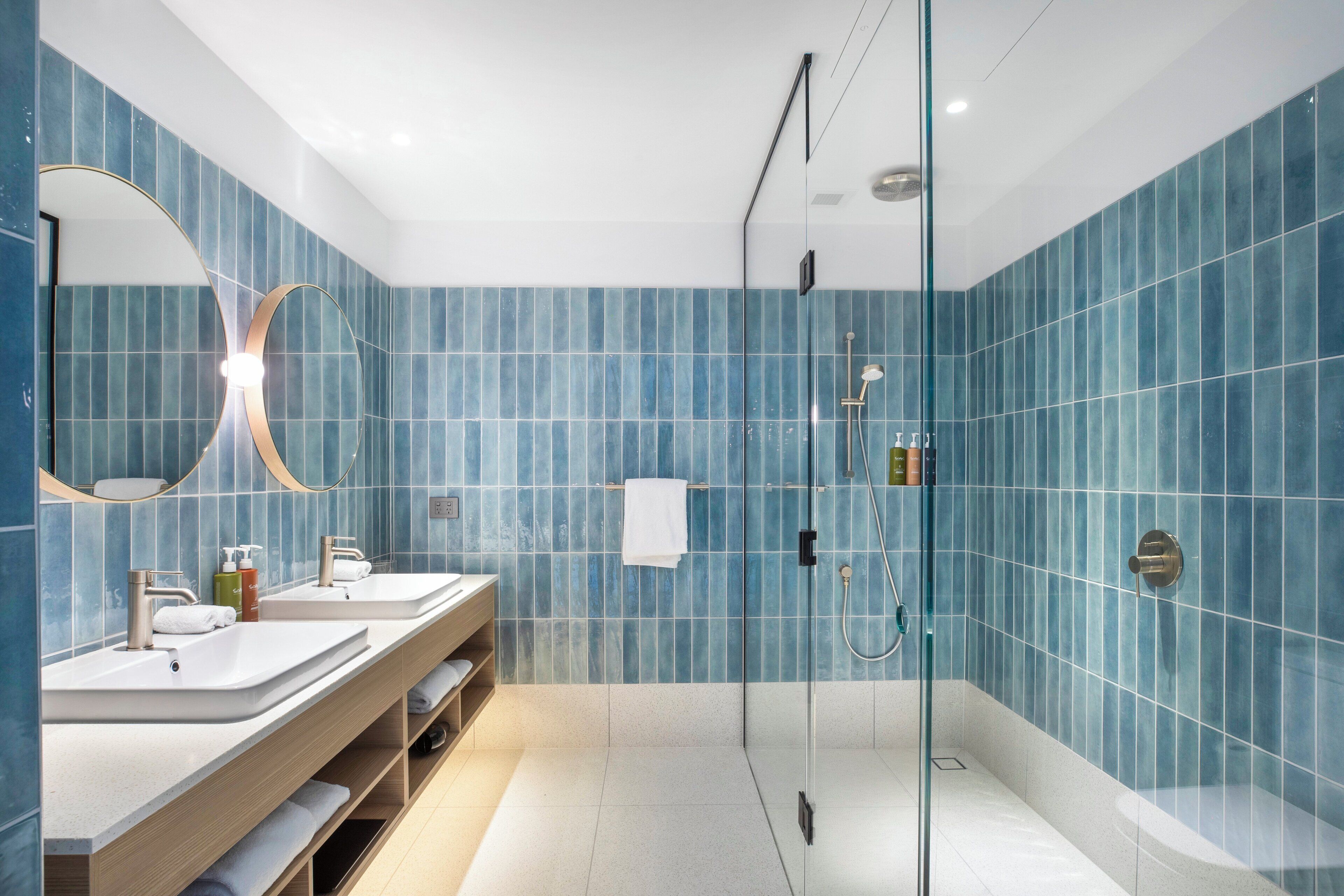 A modern bathroom with two sinks, a glass shower enclosure, and a large mirror.