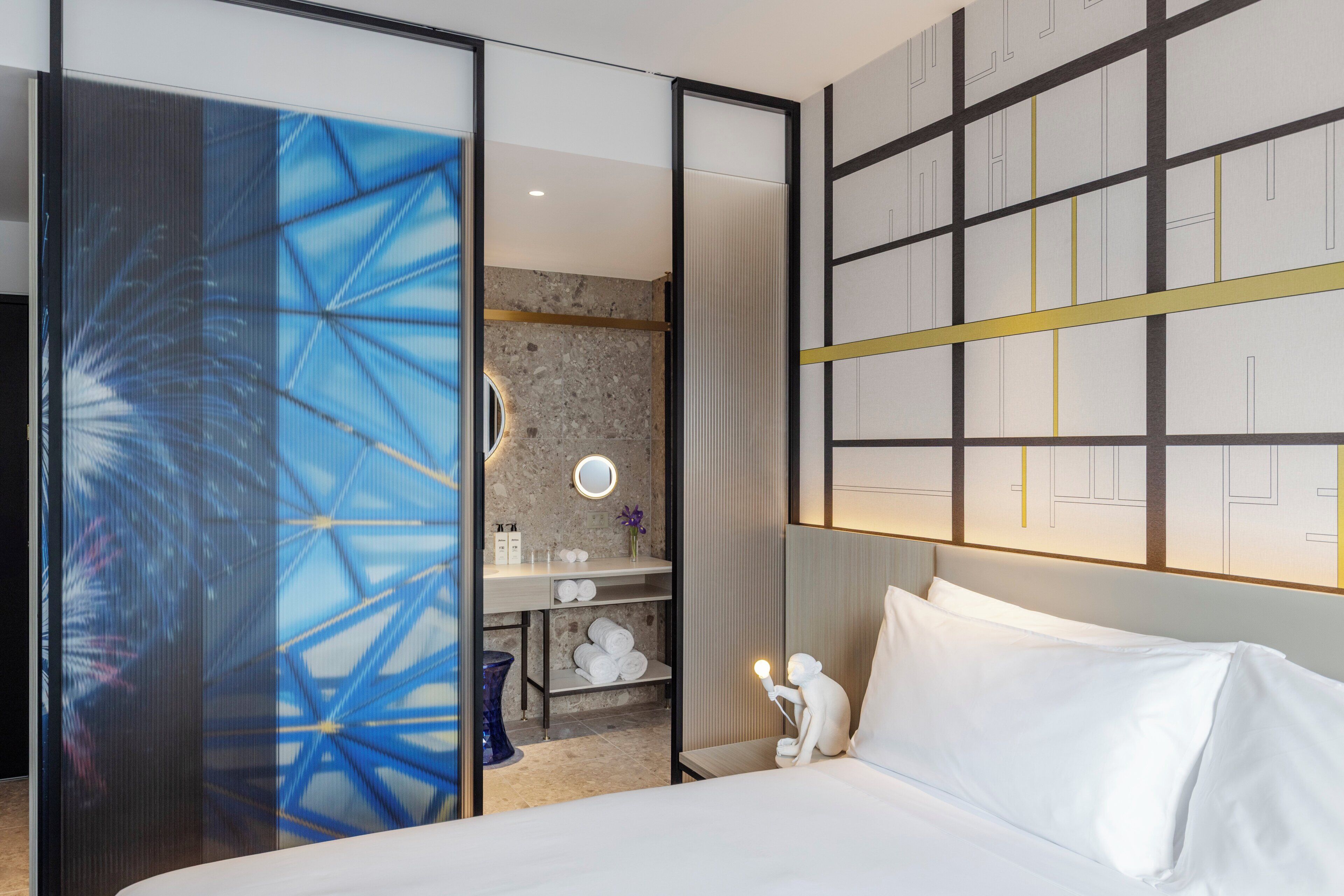 A hotel room with a bed, a bathroom with a mirror, and a wall with a geometric pattern.