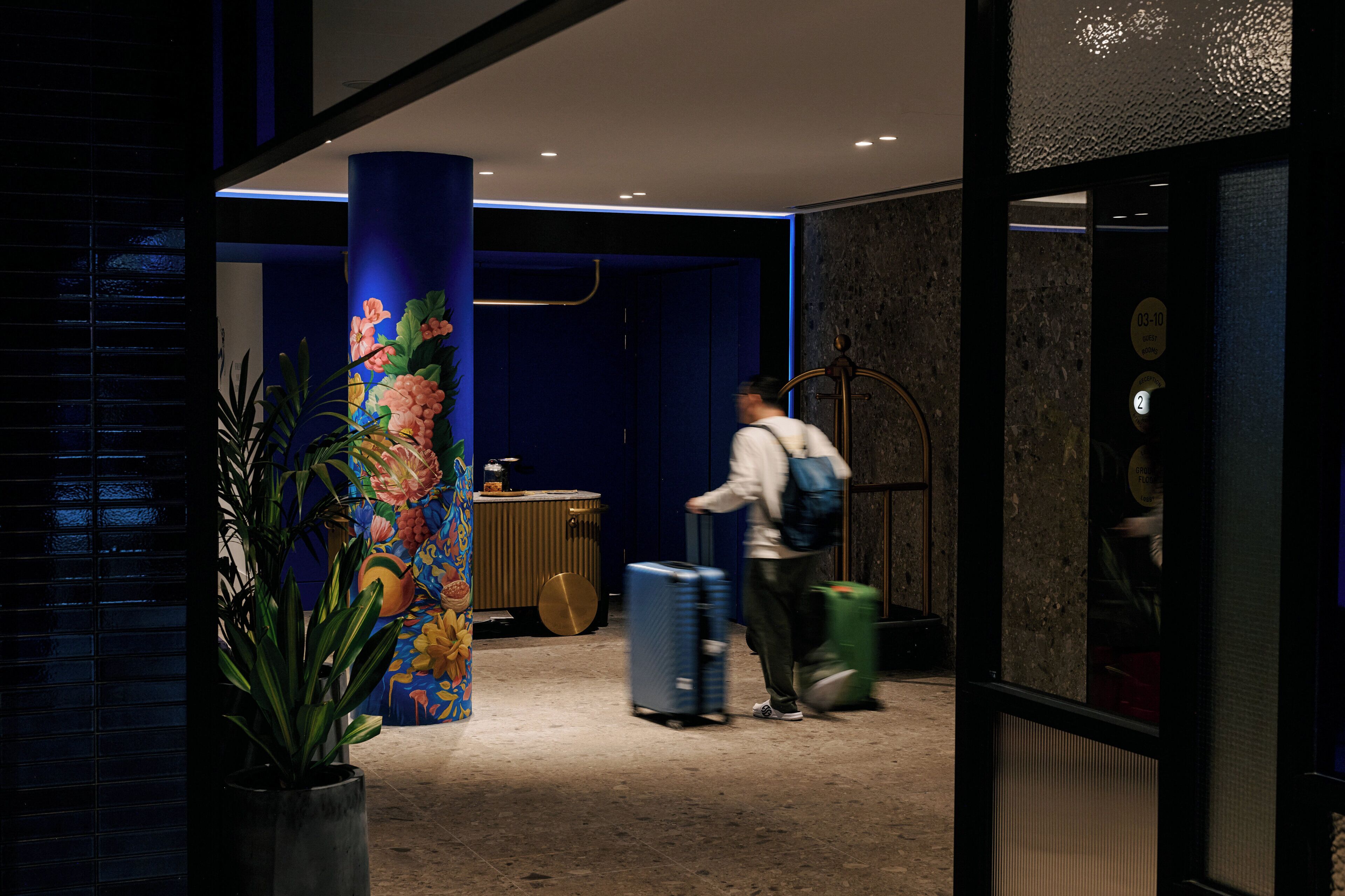 A hotel lobby with a large pillar, a reception desk, and a person with luggage.