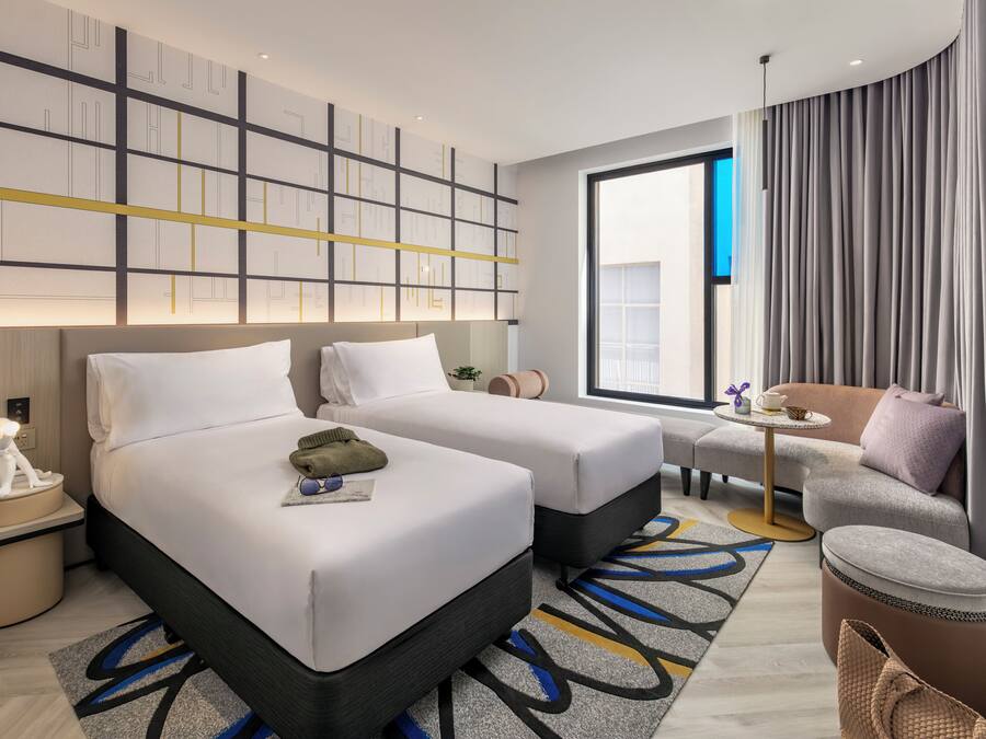 Ein modernes Hotelzimmer mit zwei Betten, einer Couch, einem kleinen Tisch und einem großen Fenster.