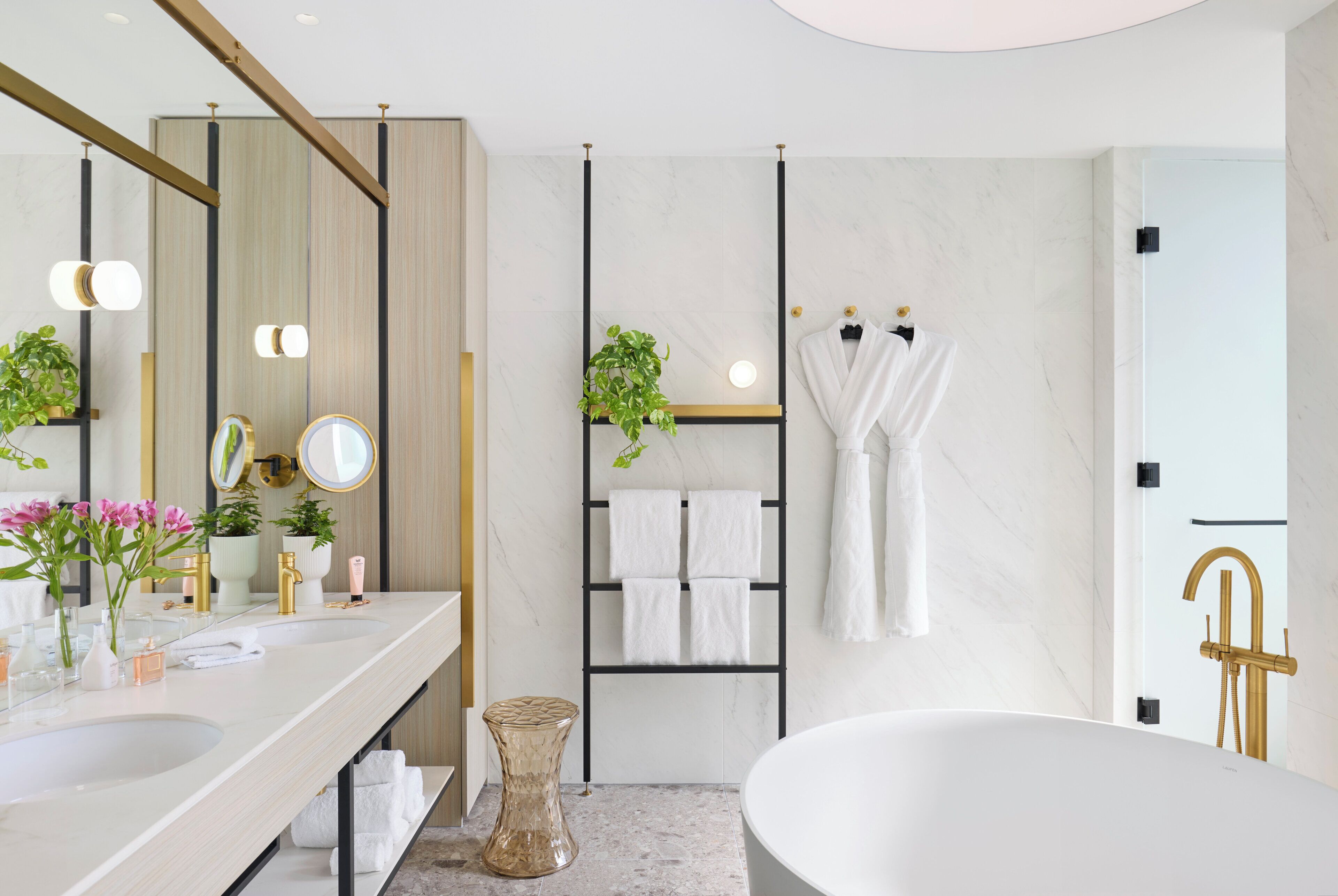 A modern bathroom with a large bathtub, a vanity with two sinks, a mirror, and a towel rack with multiple towels.
