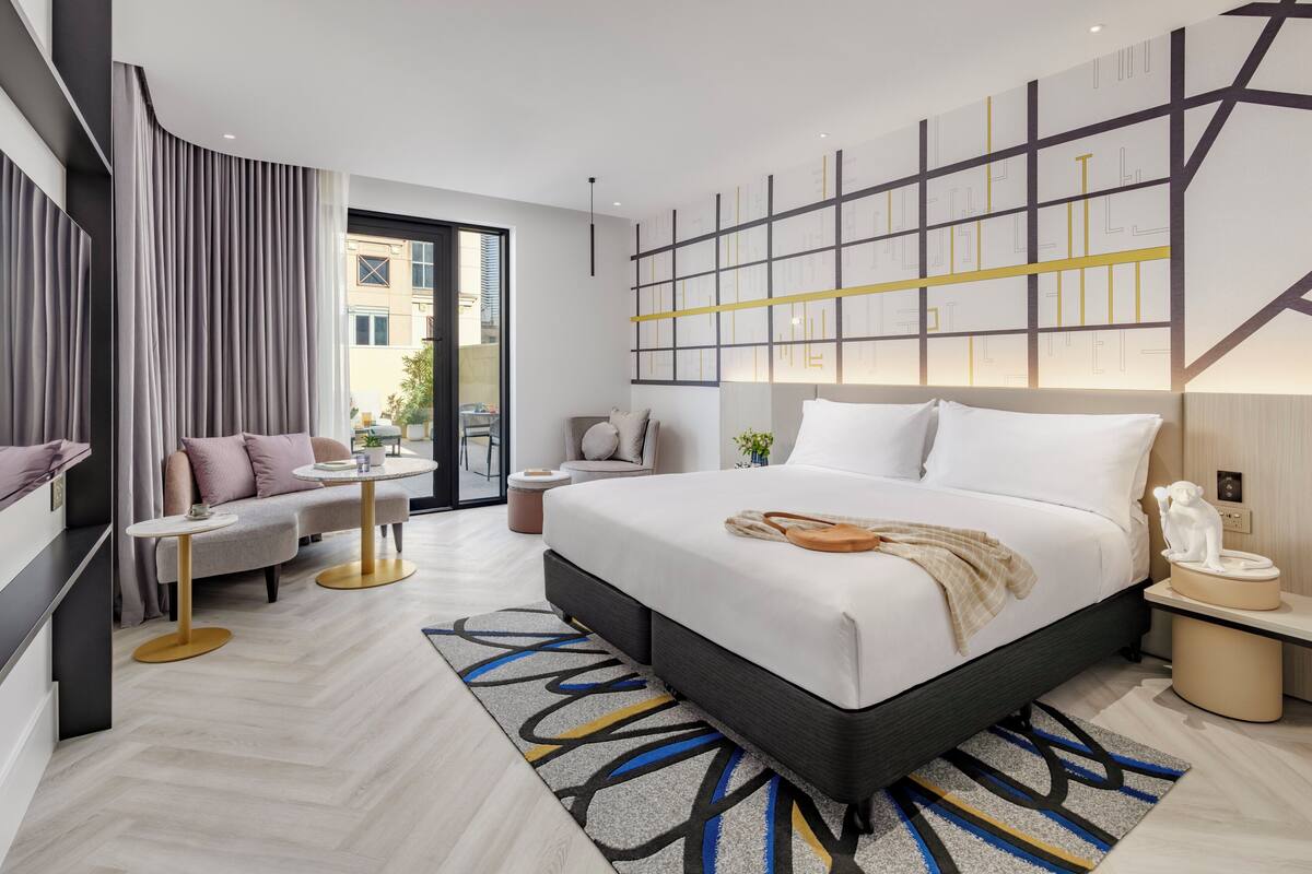 Ein modernes Hotelzimmer mit einem großen Bett, einer Couch, einem kleinen Tisch und Blick auf die Stadt.