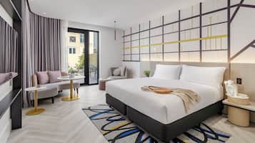 Habitación de hotel moderna con una cama grande, un sofá, una mesita y vistas a la ciudad.
