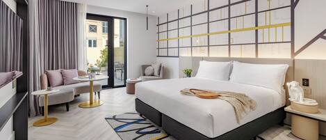 A modern hotel room with a large bed, a sofa, a small table, and a view of the city.