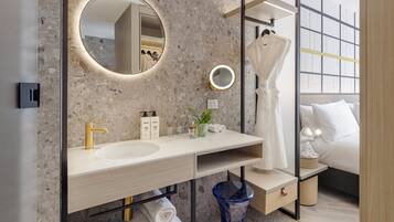 Un baño moderno con salpicadero de mármol, un espejo redondo con luces, un grifo dorado y un jarrón azul.