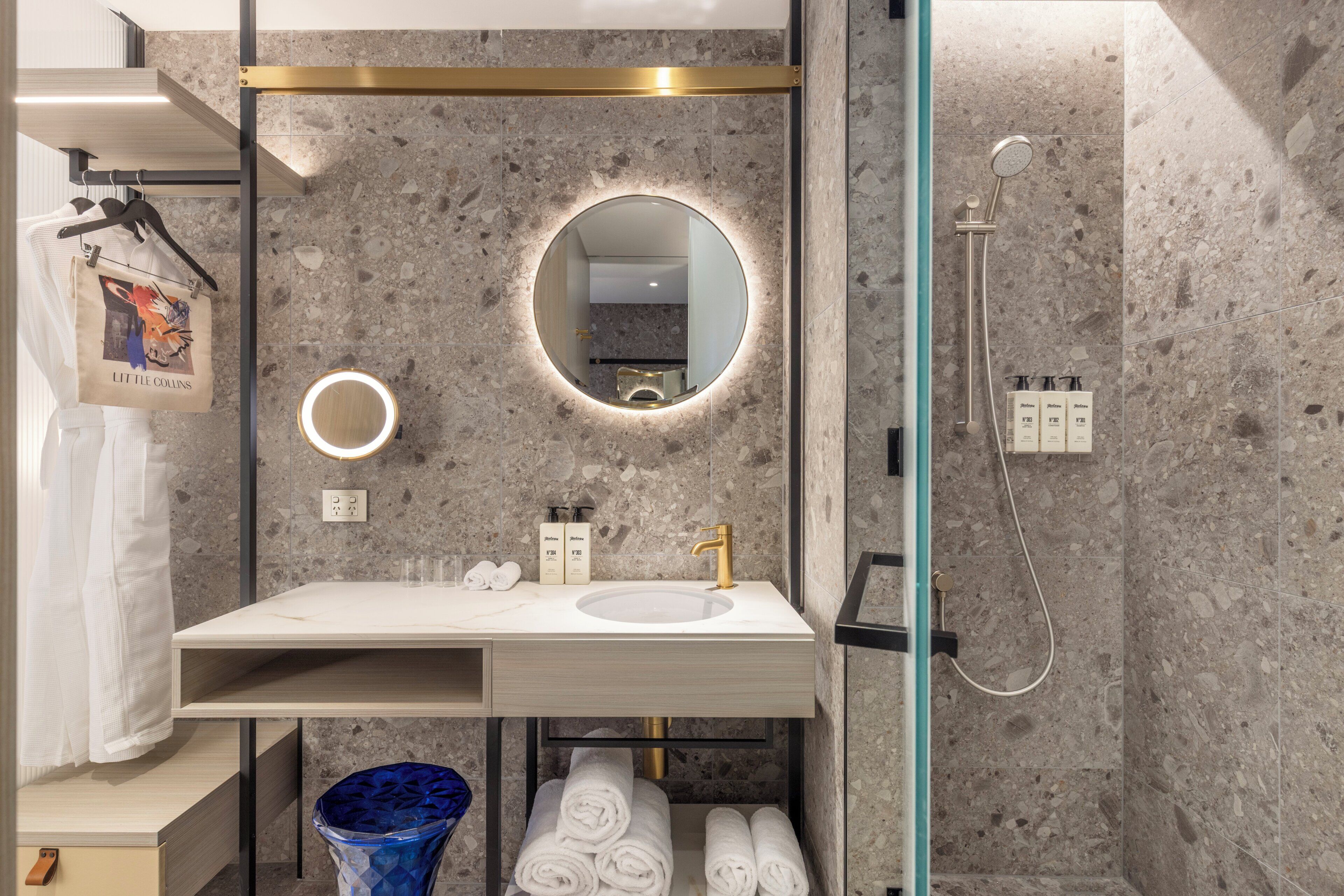 Un baño moderno con lavamanos de mármol, grifo dorado, espejo redondo con luz e hidromasaje.