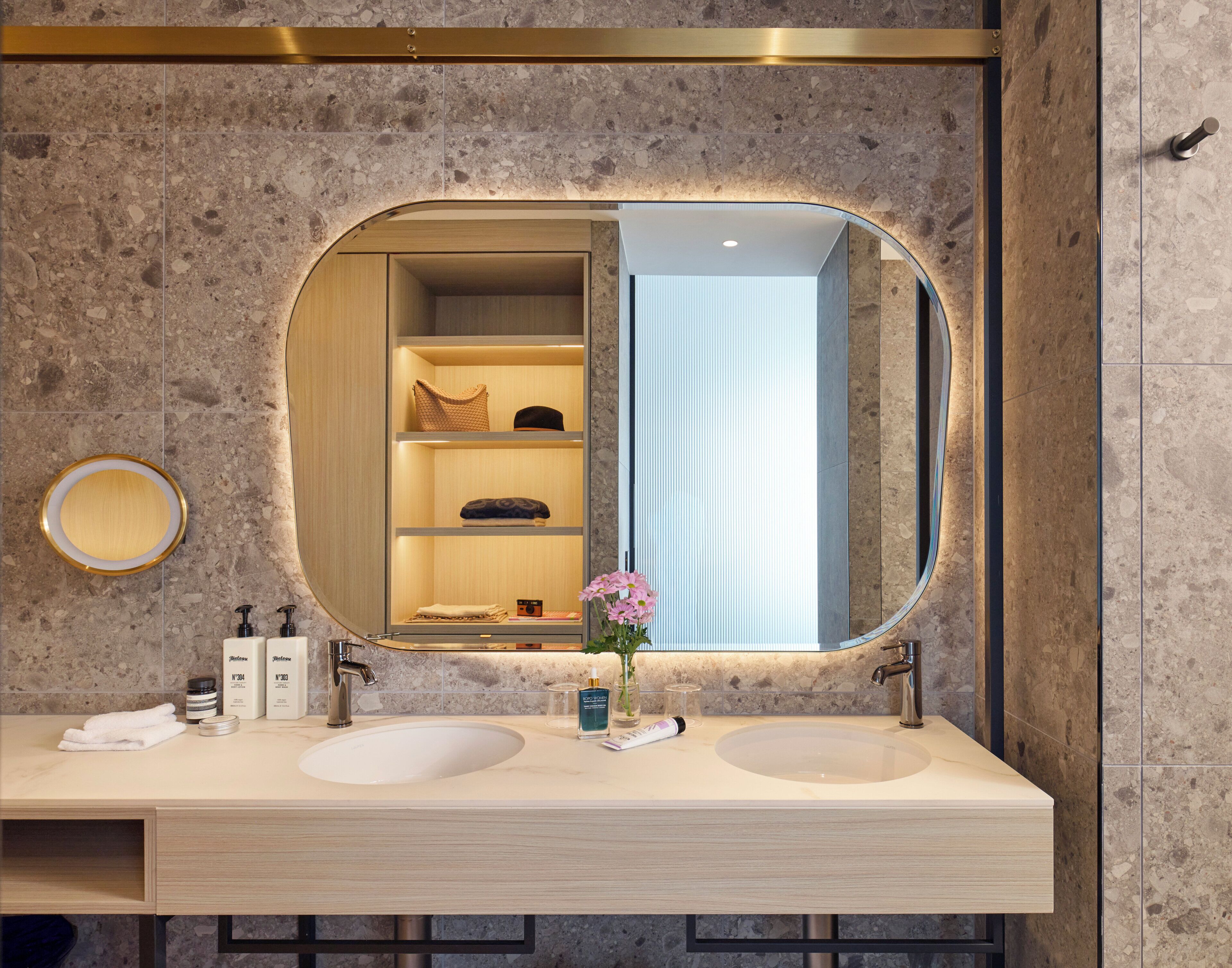 Un baño moderno con dos lavamanos, un espejo grande y un estante empotrado con artículos de aseo.
