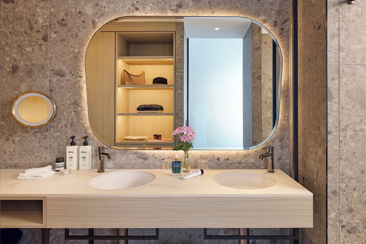 Ein modernes Badezimmer mit zwei Waschbecken, einem großen Spiegel und einer eingebauten Ablage mit Toilettenartikeln.