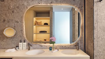 Un baño moderno con dos lavamanos, un espejo grande y un estante empotrado con artículos de aseo.