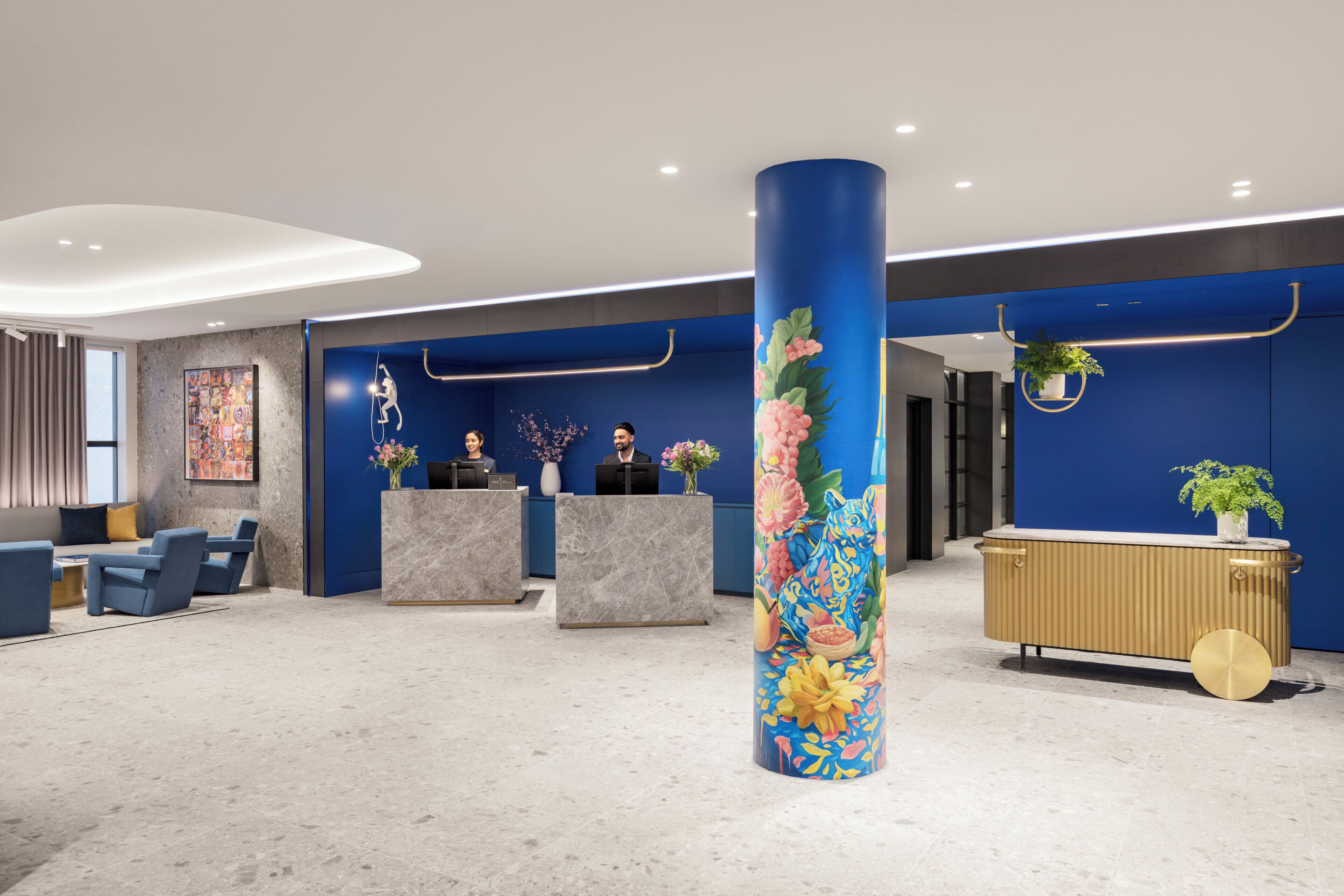 A modern reception area with a blue accent wall, marble reception desks, and a central decorative column.