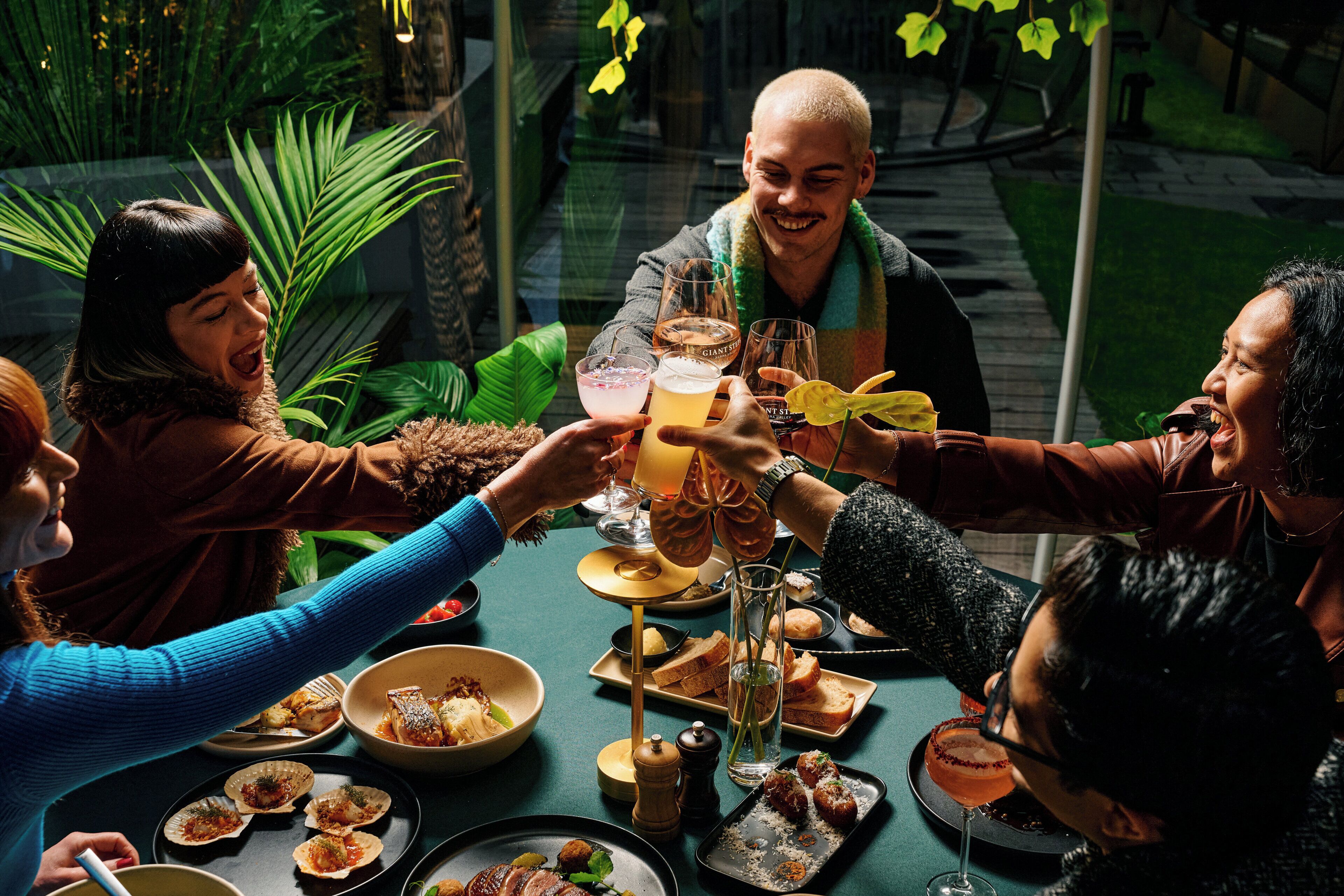 A group of people toasting at a table with various dishes and drinks.