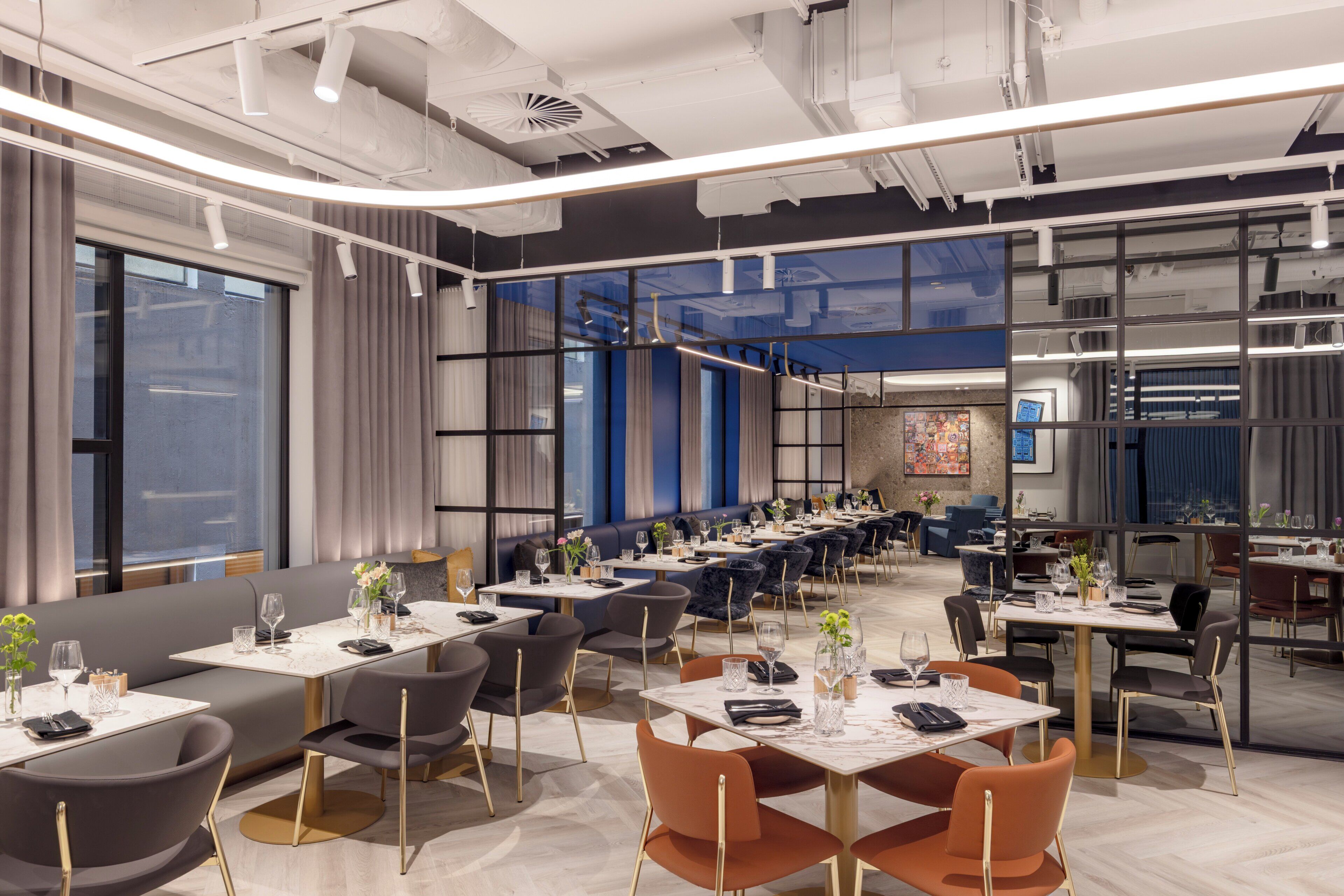 A modern dining area with tables and chairs, large windows, and a blue accent wall.