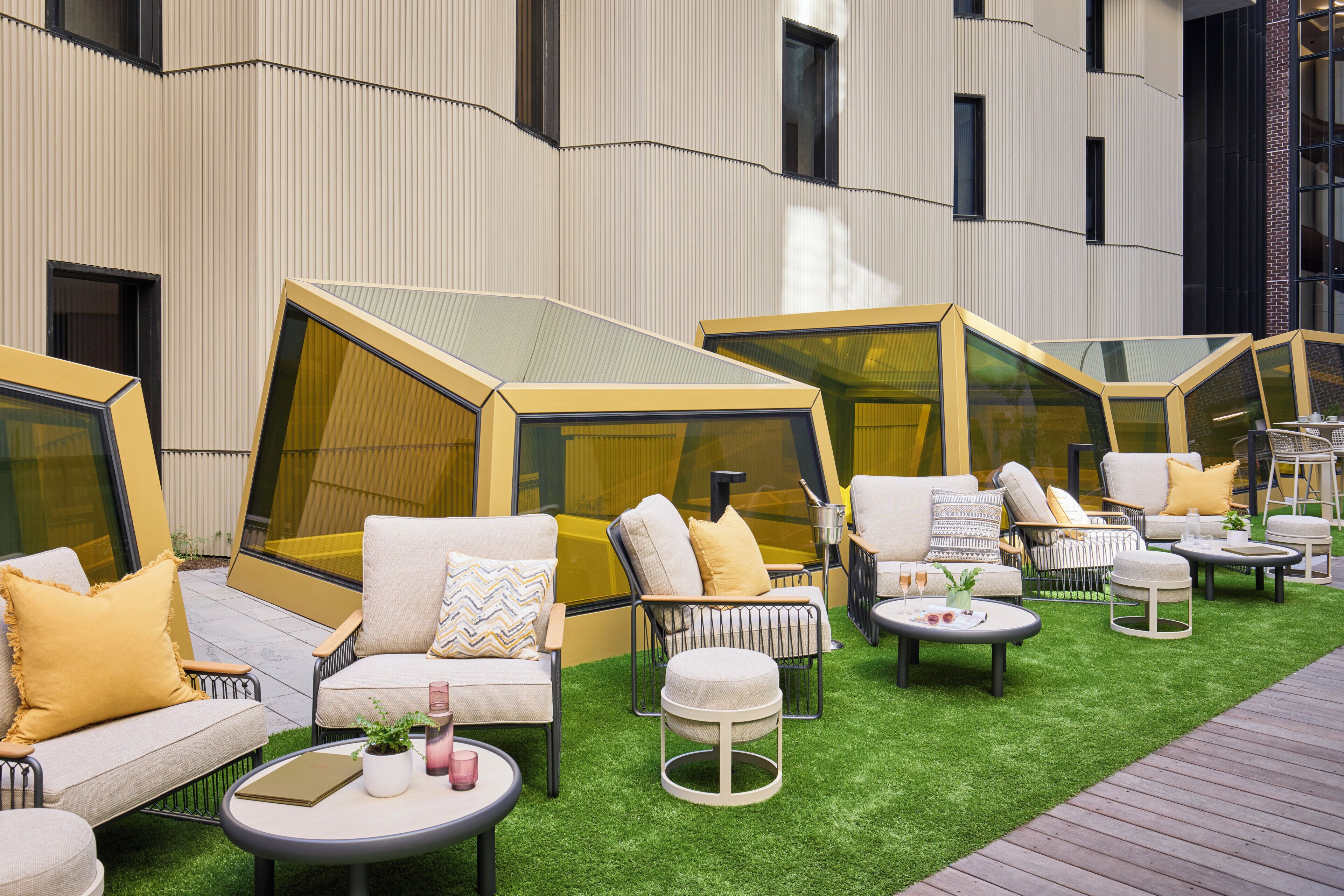 A modern outdoor seating area with geometric canopies, cushioned seating, and small tables.