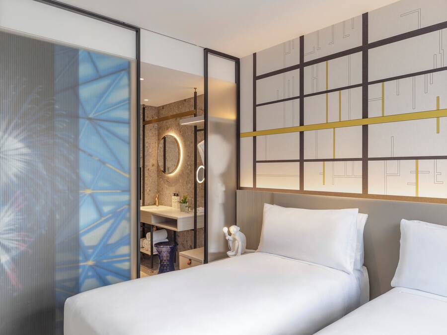 Ein modernes Hotelzimmer mit einem großen Bett, einem Badezimmer mit Spiegel und Waschbecken sowie einer dekorativen Wandverkleidung.