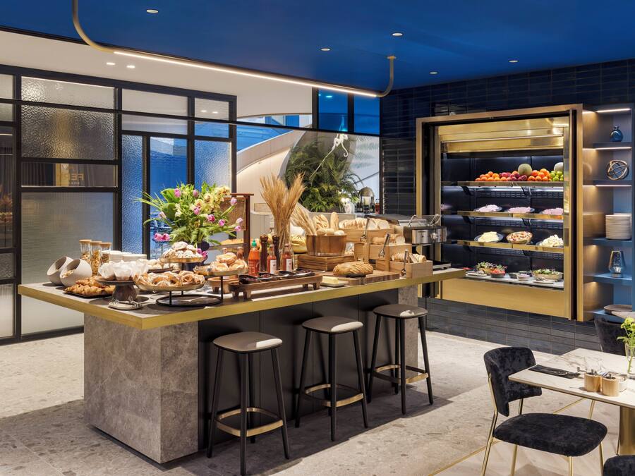 A modern bar area with a marble countertop, stools, and a variety of food and drink options.