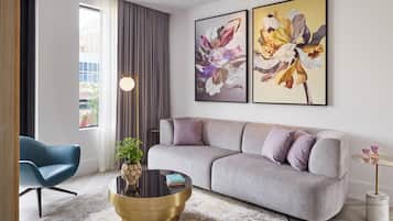 Una sala de estar moderna con un sofá gris, un sillón azul, una mesa de centro redonda y dos cuadros con motivos florales en la pared.