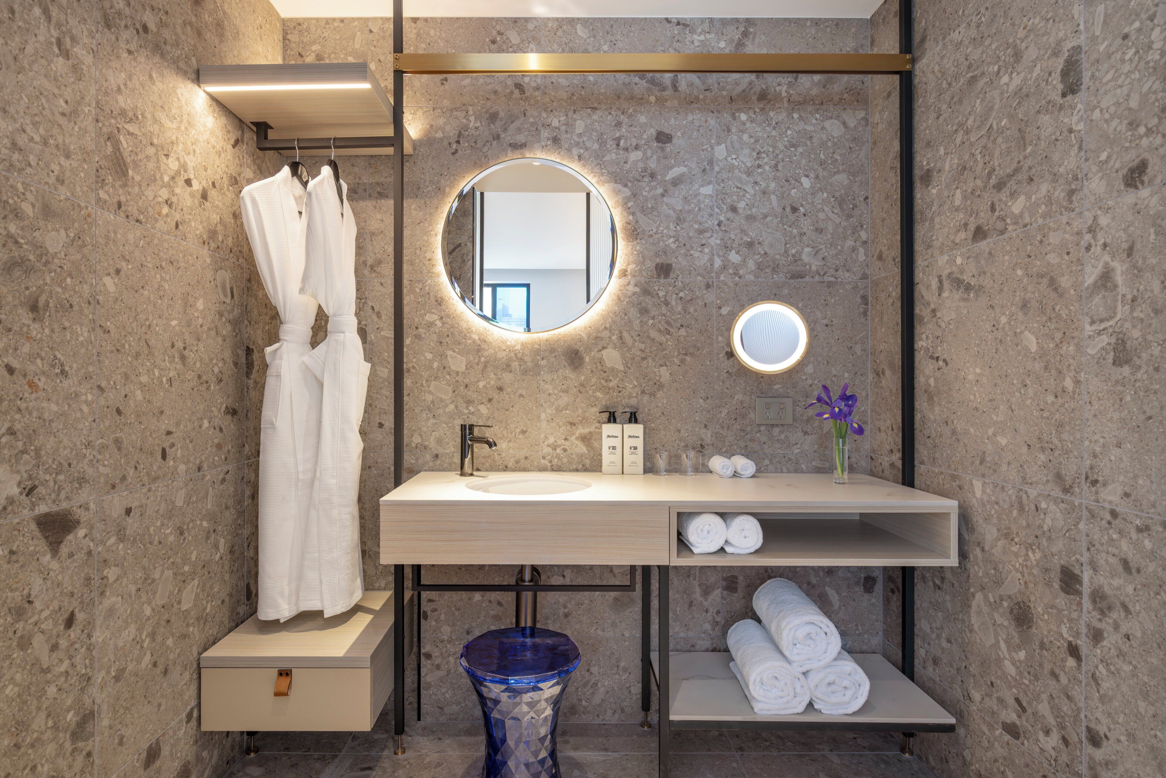 A modern bathroom with a marble wall, a round mirror, a sink, and a towel rack.