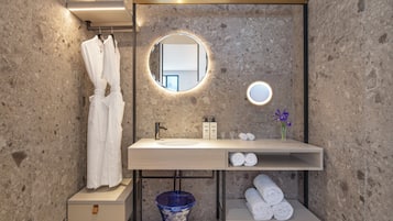 A modern bathroom with a marble wall, a round mirror, a sink, and a towel rack.