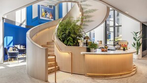 Un moderno vestíbulo de hotel con una escalera curva, una recepción y una gran planta de interior.