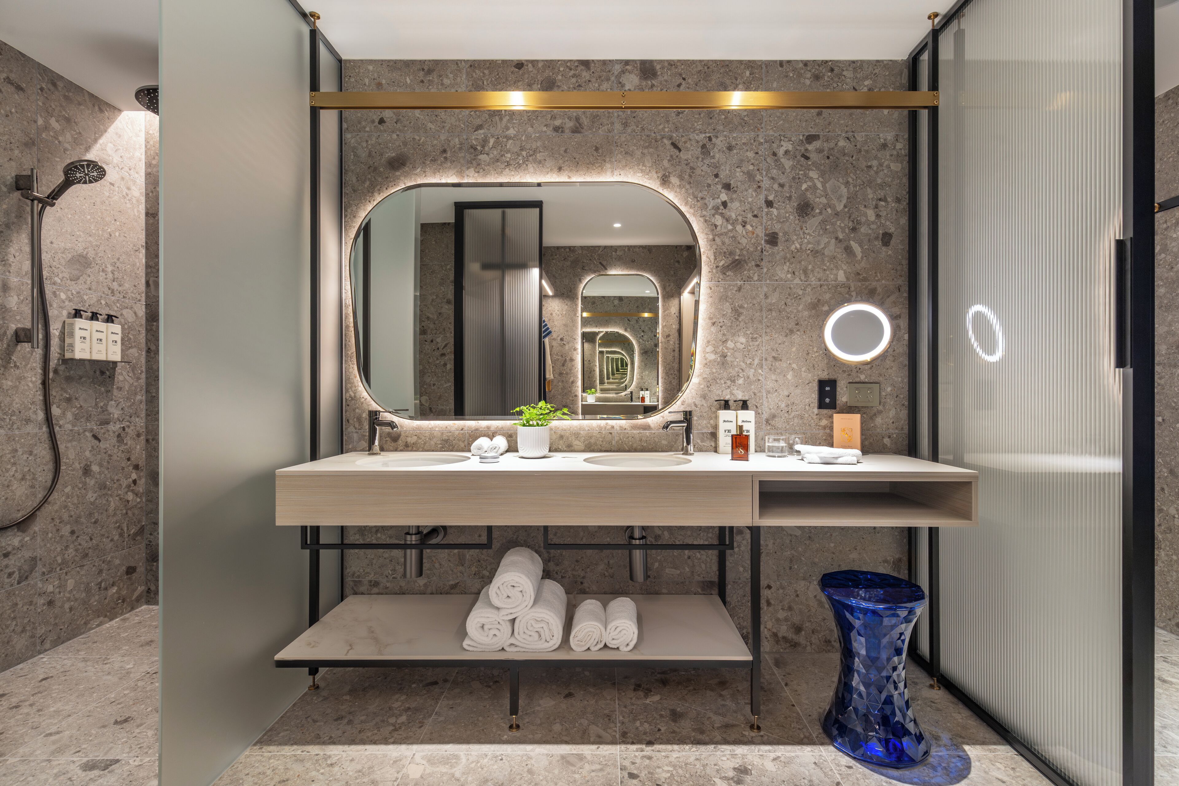 Een moderne badkamer met een grote spiegel, dubbele wastafels, een douche en een blauwe vaas.