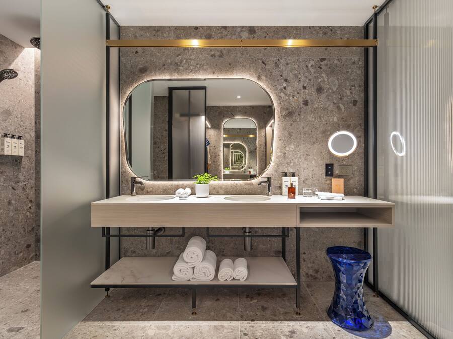 A modern bathroom with a large mirror, dual sinks, a shower, and a blue vase.