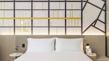 A hotel room with a large bed, a nightstand with a vase of flowers, a wall-mounted night lamp, and a decorative statue.