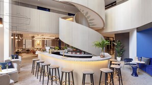 Un área de bar moderna con una escalera espiral, taburetes y una zona de estar con mesas y sillas.