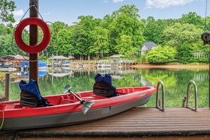 Un canoë rouge est amarré à un quai, avec une bouée de sauvetage à proximité. Le lac est calme, et on aperçoit un bateau amarré au loin.