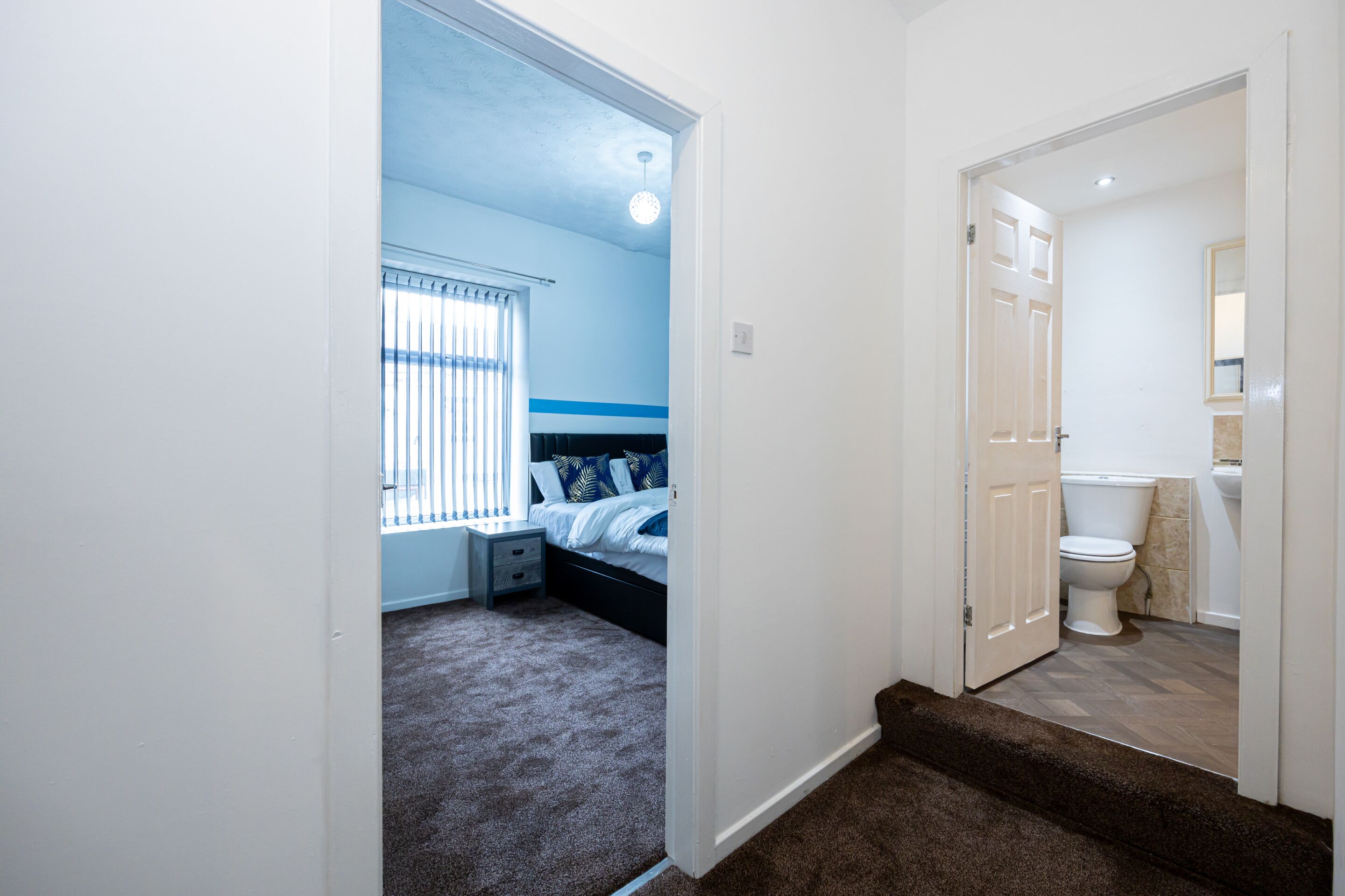 A bedroom with a bed, a nightstand, and a window with blinds.