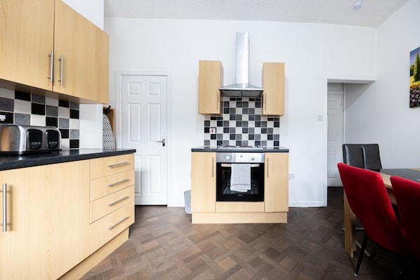A compact kitchen with wooden cabinets, a black countertop, and a tiled backsplash. - Barnes Street Terrace (Accrington, Lancashire, United Kingdom)