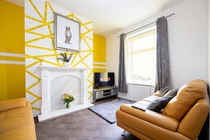 A living room with a fireplace, a sofa, a television, and a window with curtains. - Barnes Street Terrace (Accrington, Lancashire, United Kingdom)