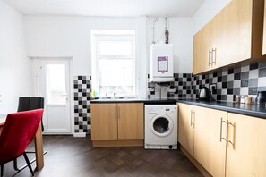 A compact kitchen with a washing machine, wooden cabinets, and a checkered backsplash. - Barnes Street Terrace (Accrington, Lancashire, United Kingdom)