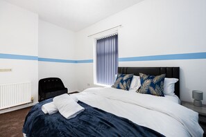 A hotel room with a neatly made bed, a chair, a window with blinds, and a bedside table with a lamp. - Barnes Street Terrace (Accrington, Lancashire, United Kingdom)