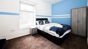 A bedroom with a bed, a nightstand, a wardrobe, and a window with blinds. - Barnes Street Terrace (Accrington, Lancashire, United Kingdom)