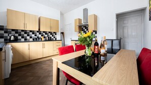 A modern kitchen with wooden cabinets, a black and white checkered backsplash, a dining table with red chairs, and a vase with flowers. - Barnes Street Terrace (Accrington, Lancashire, United Kingdom)
