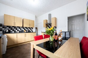 A modern kitchen with wooden cabinets, a black and white checkered backsplash, a dining table with red chairs, and a vase with flowers. - Barnes Street Terrace (Accrington, Lancashire, United Kingdom)